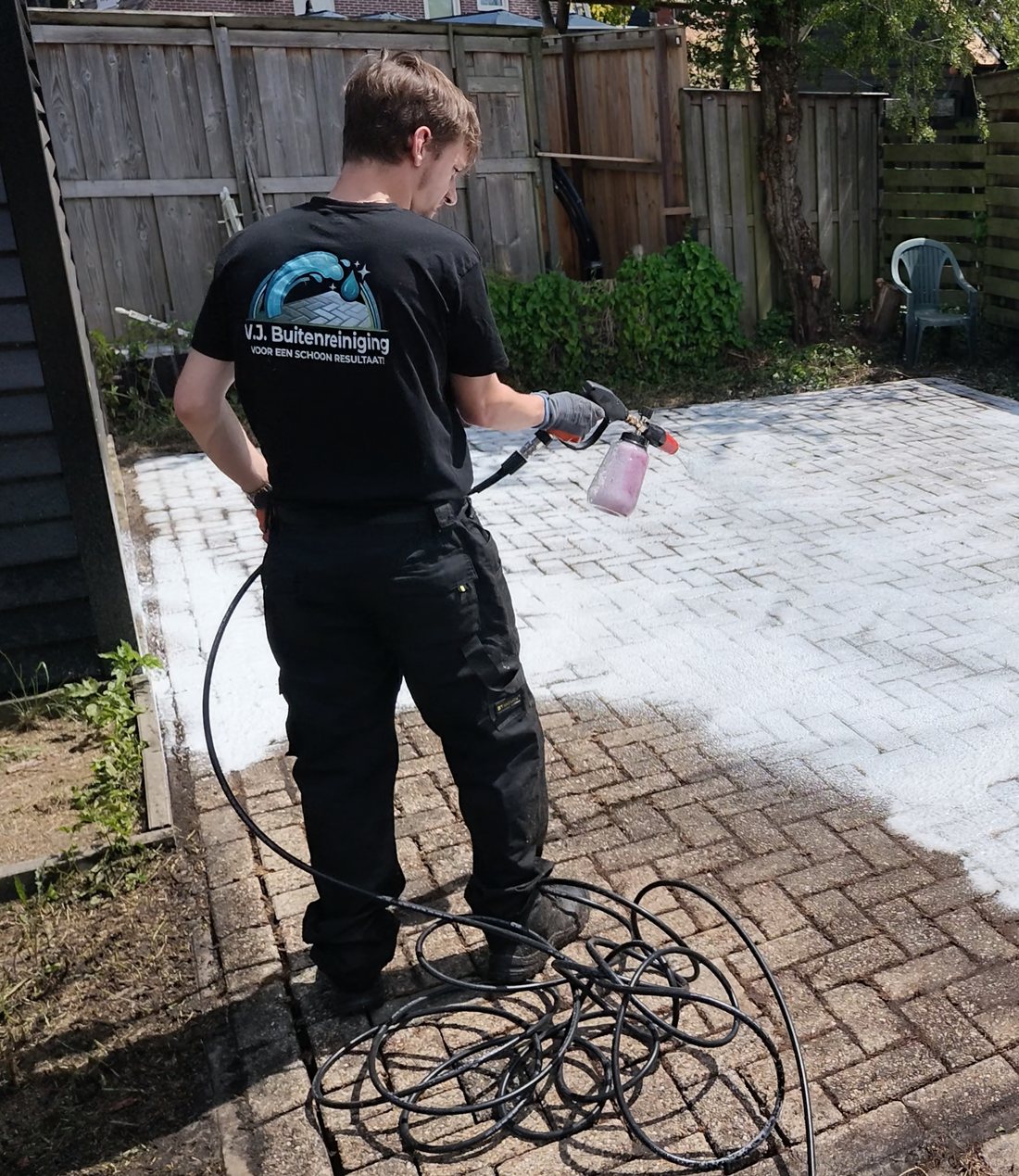 Medewerker van V.J. Buitenreiniging brengt reinigingsschuim aan op een terras